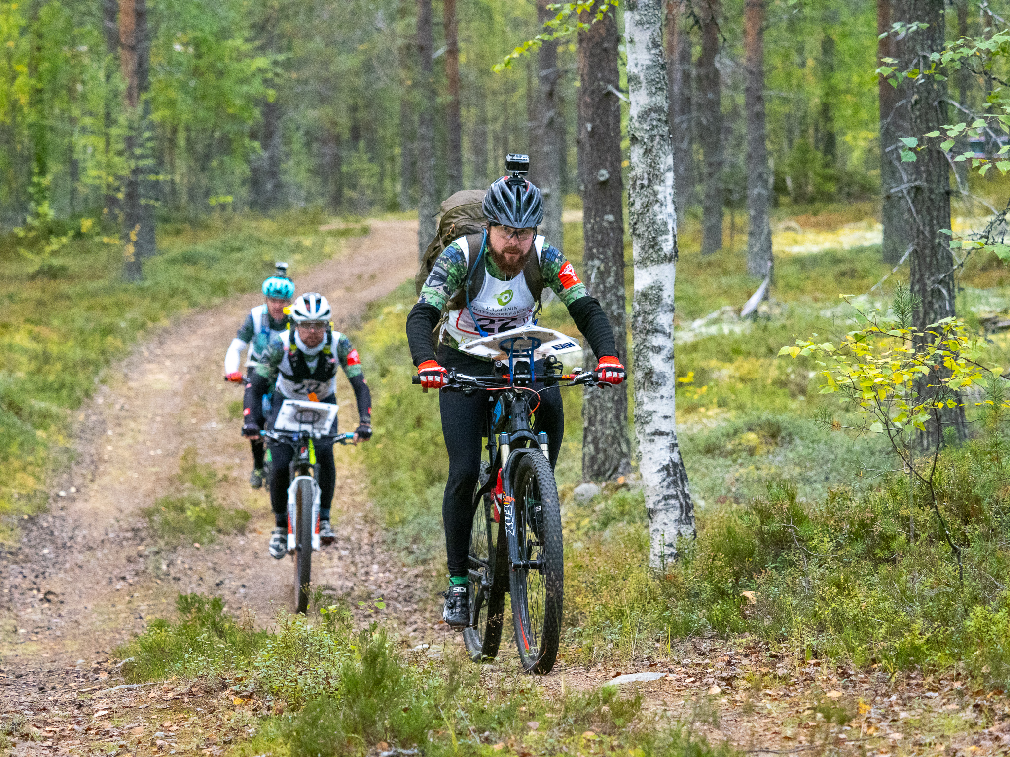Kaksi pyöräilijää pyöräilee pururadalla metsässä.