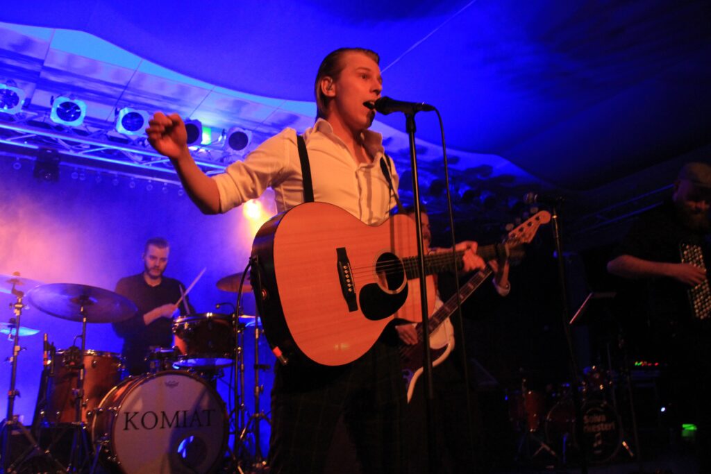 Komiat Official laulaja kitarakädessä ja mikrofoni edessä.