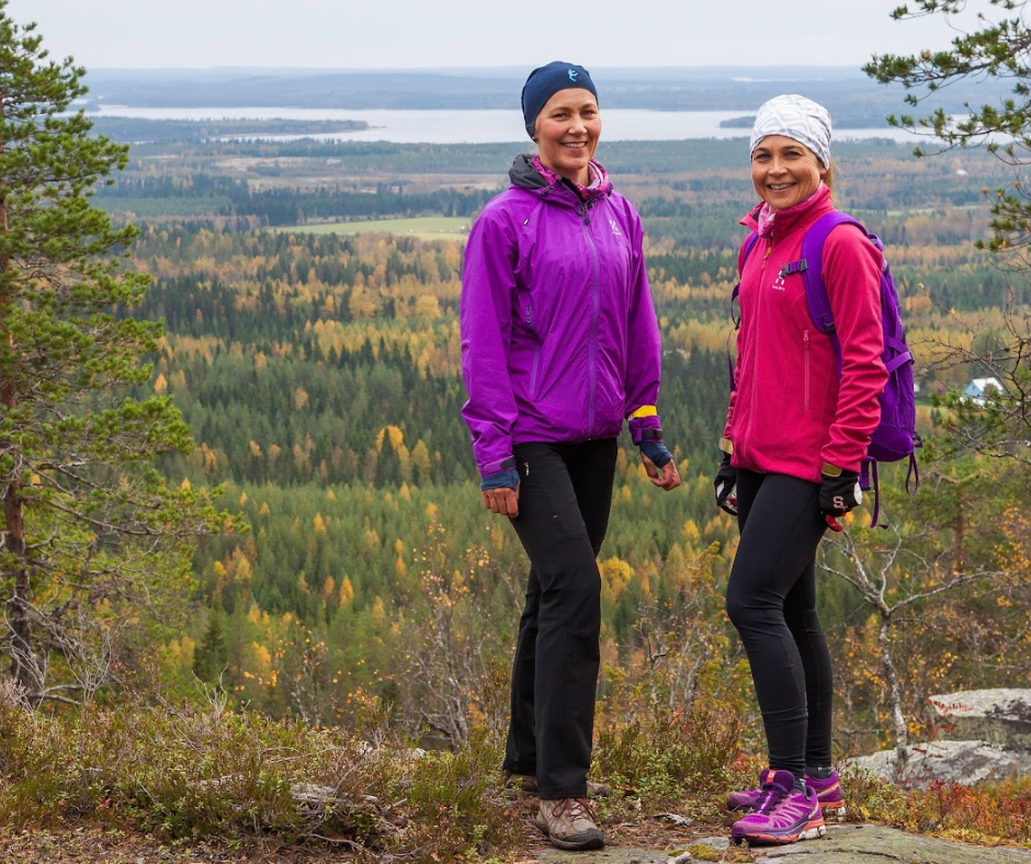 Kaksi henkilöä seisoo kalliolla. Vuokatin syksyinen vaaramaisema taustalla.
