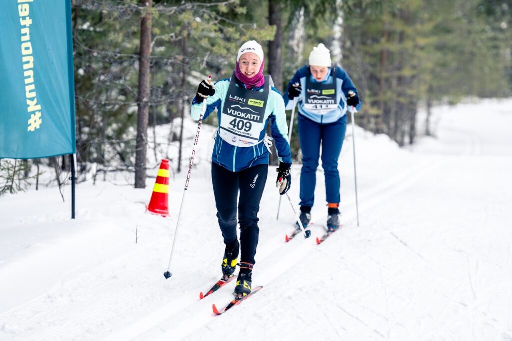 Kaksi hiihtäjää talvisessa maisemassa metsässä.