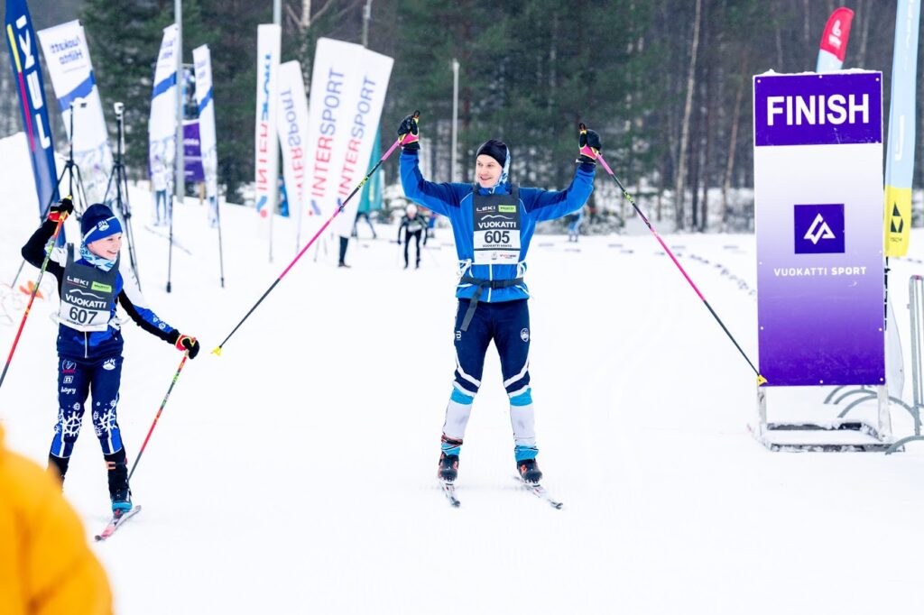 Kaksi hiihtäjää saapuu maaliin ja tuulettavat kädet ilmassa.